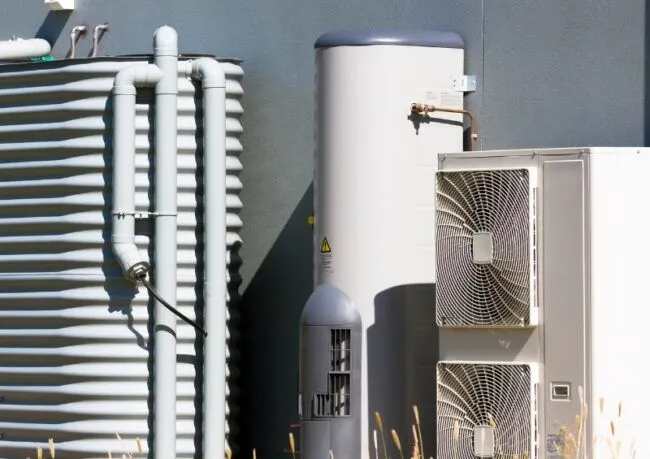 Hot Water Repair showing an outdoor heat pump hot water system with storage tank, pipes, and condenser unit