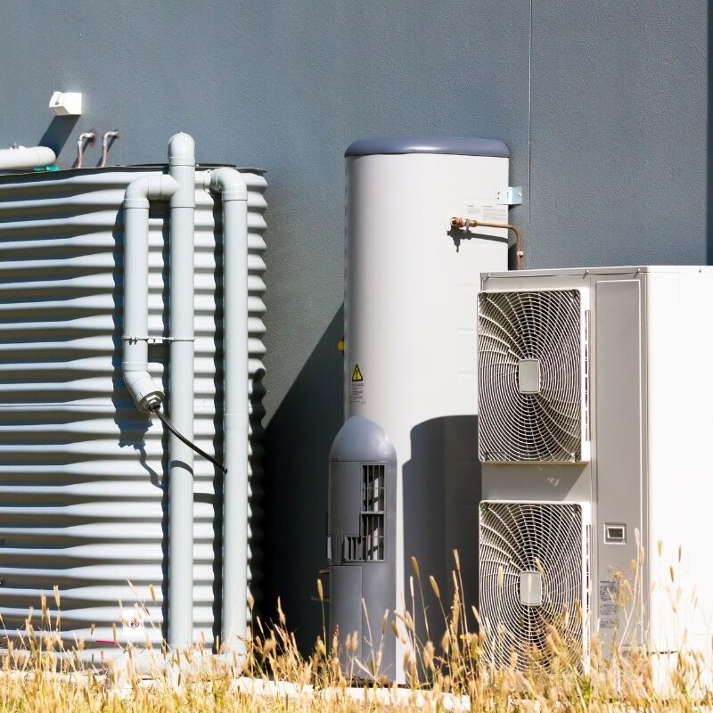 Hot Water Repair showing an outdoor heat pump hot water system with storage tank, pipes, and condenser unit