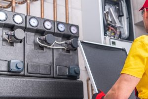 Technician in a yellow shirt and red gloves inspecting a gas hot water heater system with pressure gauges, addressing issues of gas hot water not working.