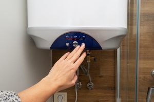 Hand adjusting the temperature on a water heater, showing the importance of knowing when to replace a water heater.