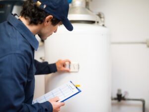 Licensed plumber inspecting a Rheem water heater during rheem installation and checking the thermostat settings with a clipboard.