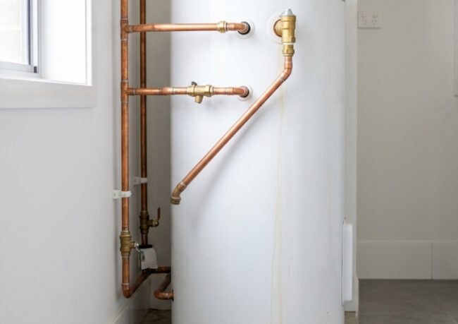 Ageing residential hot water system with minor water pooling at the base in a clean Australian home utility area.